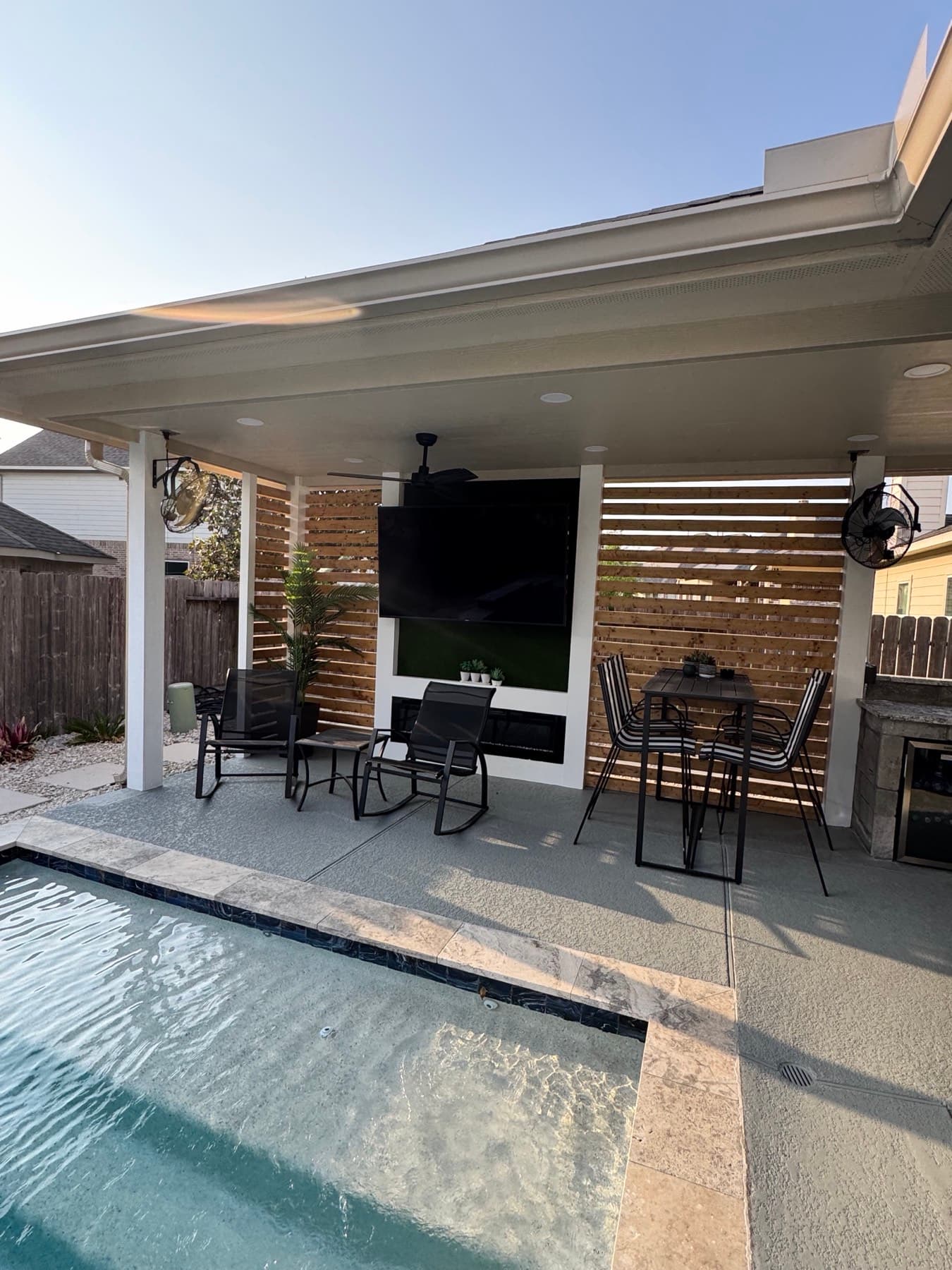 Poolside covered patio with a wall-mounted weatherproof television and outdoor fans